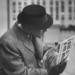 Man reading a newspaper while wearing a Fedora hat with a flatte